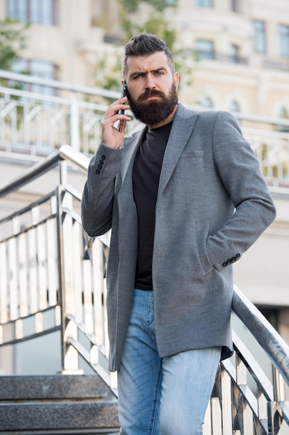 Stay in touch Man bearded serious businessman hold mobile phone urban background Hipster smartphone call partner Man mobile call smartphone Mobile call concept Important mobile conversation