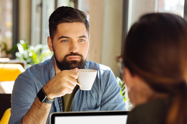 集中し続ける。一杯のコーヒーで彼の反対側に座っている間彼の同僚を見ている真面目な集中男