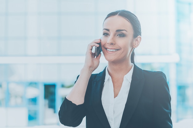 Staying connected. Beautiful young woman in formalwear talking on the mobile phone and smiling while standing outdoors