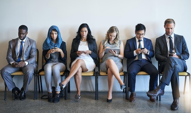 Фото Оставайтесь на связи, пока они ждут группа хорошо одетых бизнесменов, использующих свои смартфоны в ожидании интервью