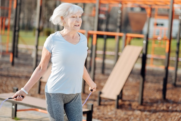 Staying fit. Joyful thin woman jumping rope while exercising in the open air