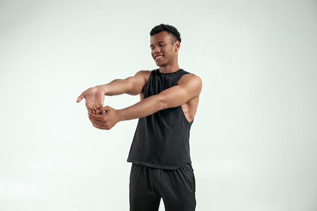 Staying flexible strong young afro american man warming up while standing against grey background