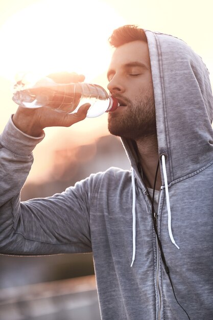 Staying hydrated. Confident young man drinking water while standing outdoors