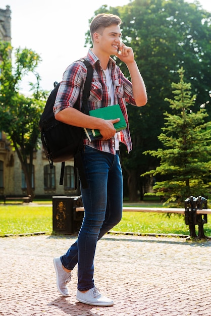 Staying in touch with friends. Full length of handsome male student talking on the mobile phone and smiling while walking outdoors