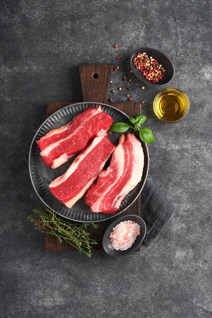 Steak beef Raw steak New York with rosemary and spices on old iron plate on old dark stone background Top view Mock up