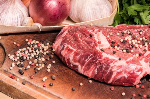 Photo steak of beef on a wooden board with spices pepper parsley salt onions shallots garlic