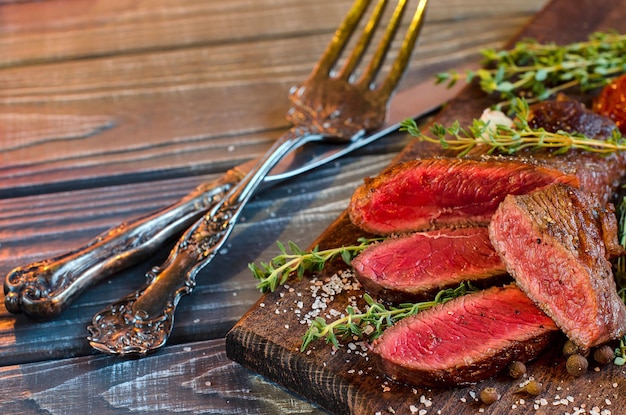 Steak kookmedium Steak in plakjes gesneden Donkere keuken Bord Vintage mes en vork