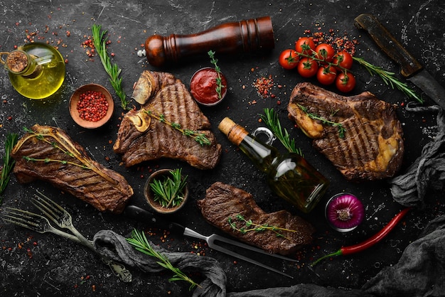 Steak menu. Juicy grilled steaks on a black stone background: t-bone, striploin, Rib eye, new york steak. Top view. Rustic style.