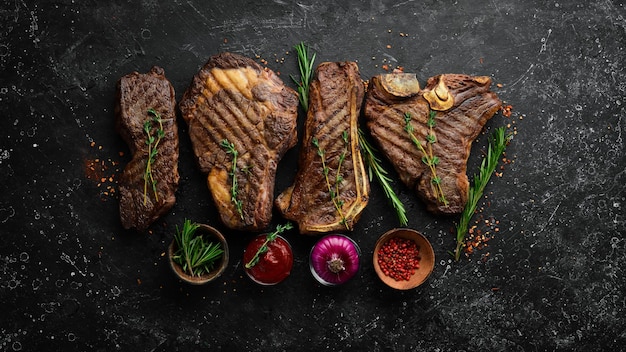 Steak menu Juicy grilled steaks on a black stone background tbone striploin Rib eye new york steak Top view Rustic style