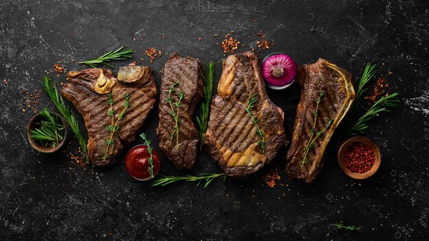 Стейк-меню Сочные стейки на гриле на фоне черного камня tbone striploin Рибай нью-йоркский стейк Вид сверху Деревенский стиль