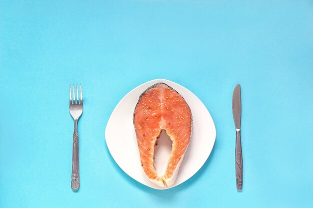 ナイフとフォークで白い皿に赤い魚のマリネステーキの部分。