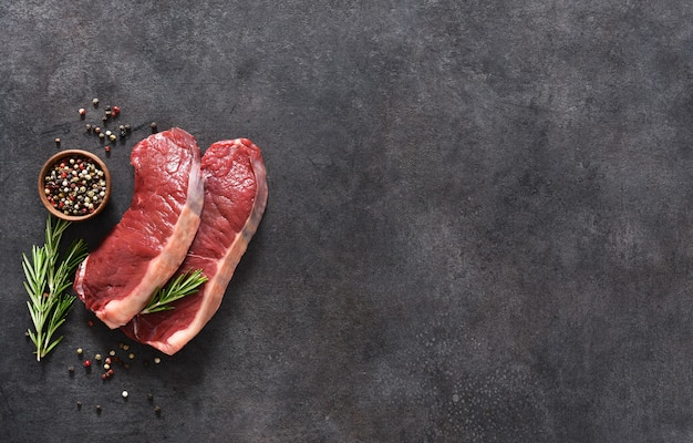 Steak, raw beef with spices and rosemary on a black concrete background. View from above.