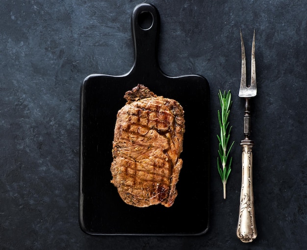 Steak Ribeye on a black cutting board rosemary and metal vintage fork
