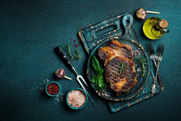 steak ribeye grilled with pepper garlic salt and thyme served on a cutting board on a dark stone background Top view with copy space Flat lay