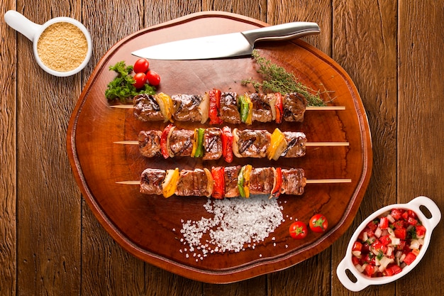 Steak skewers on top of a board with vinagrete and corn flour