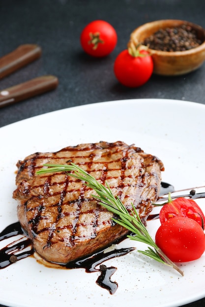 Steak on white plate with cherry tomato and rosemary close up