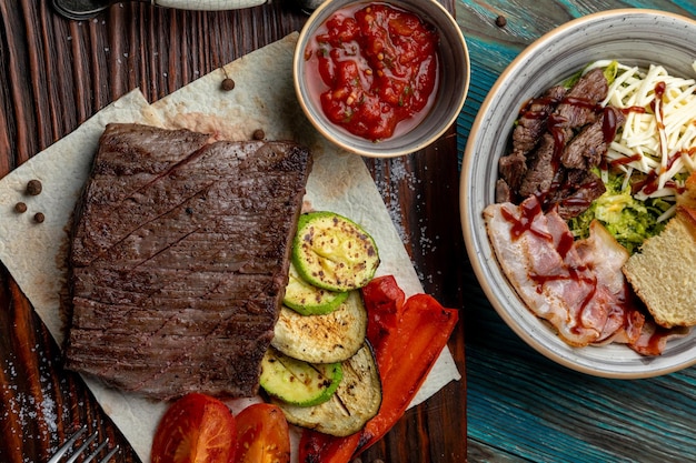 Steak with grilled vegetables served on a wooden tray with sauce