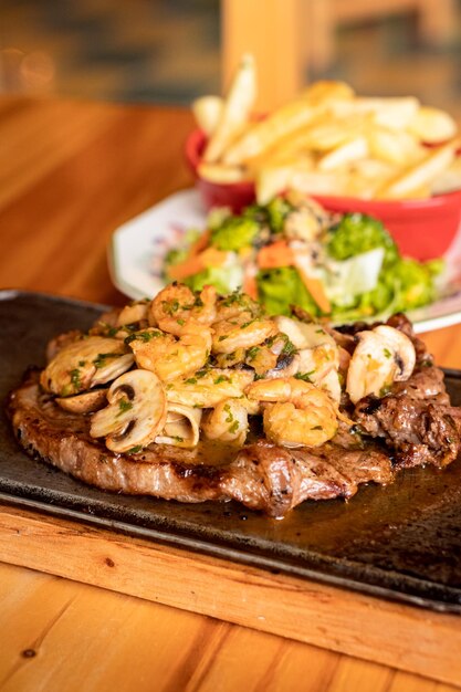 Foto una bistecca con gamberi e patatine fritte su un piatto