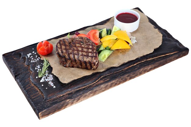 Steak with vegetables and sauce on dark wooden board, isolated on white background.