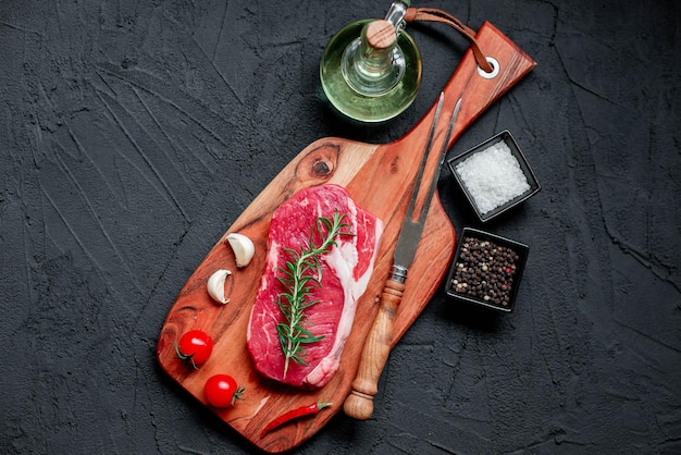 A steak on a wooden board with spices and herbs on a black background.