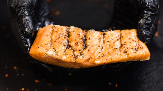 Steakhouse e ristorante di pesce. primo piano del pezzo succoso di filetto di salmone affumicato stagionato nelle mani dello chef in guanti da cucina neri.