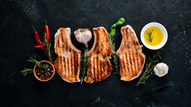 Steaks on the bone with rosemary. Grill, barbecue. On a black stone background. Top view. Free copy space.