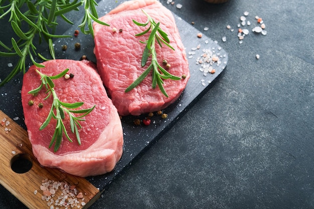 Steaks Fresh Filet mignon Steaks with spices rosemary and pepper on black marble board on gray background Top view Mock up