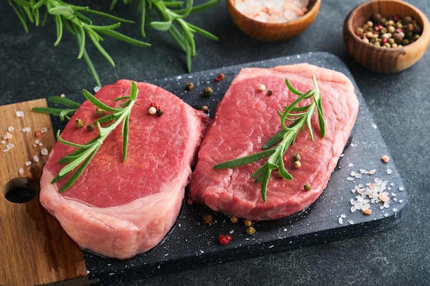 Photo steaks fresh filet mignon steaks with spices rosemary and pepper on black marble board on gray background top view mock up