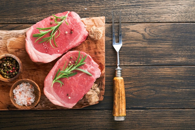 Steaks fresh filet mignon steaks with spices rosemary and\
pepper on black marble board on old wooden table background top\
view mock up