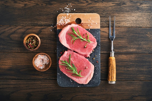 Steaks fresh filet mignon steaks with spices rosemary and\
pepper on black marble board on old wooden table background top\
view mock up