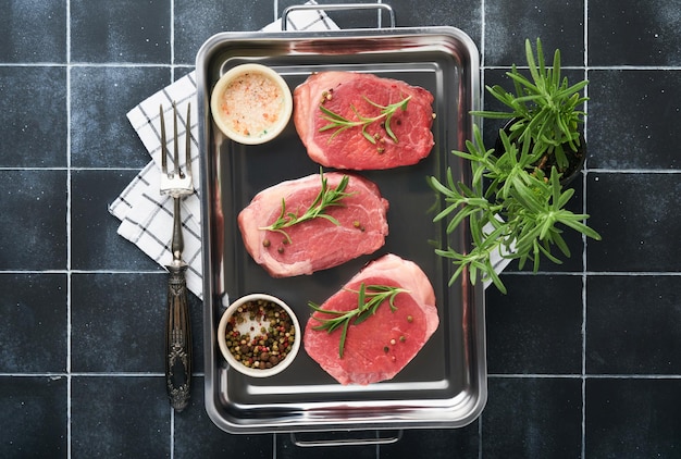 Steaks fresh filet mignon steaks with spices rosemary and\
pepper in kitchen tray on light gray background top view