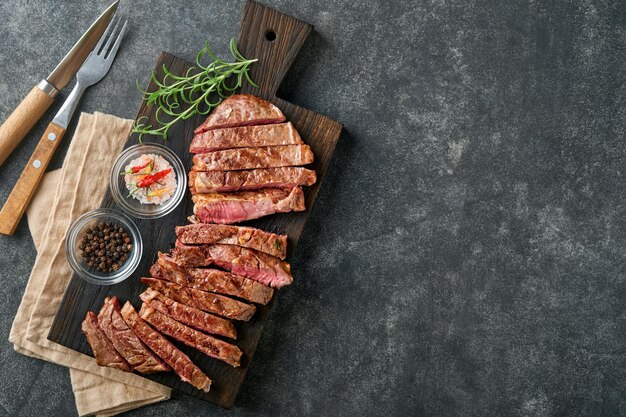 Steaks Gesneden gegrild vlees steak New York of Ribeye met kruiden rozemarijn en peper op zwart marmeren bord op oude houten achtergrond Bovenaanzicht Mock up