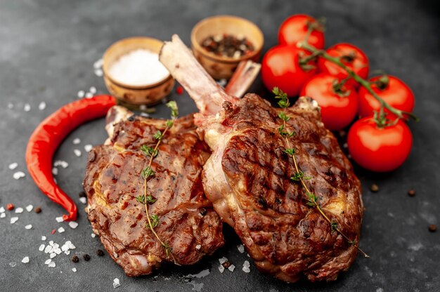steaks - grilled beef tomahawks with spices, thyme on a stone background.