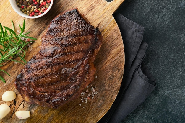 Steaks Grilled New York Steak with spices rosemary and pepper on black marble board on gray background Top view Mock up