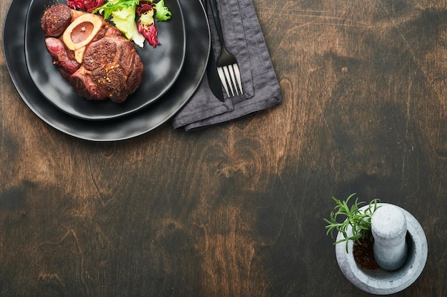 Foto bistecche osso buco fette di manzo alla griglia osso buco o bistecca di carne porterhouse con guarnito con insalata e patatine fritte su tavola di marmo nero su fondo in legno vecchio vista dall'alto mock up