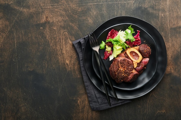 Steaks Osso Buco Sliced beef grilled Osso Buco or porterhouse meat steak with garnished with salad and french fries on black marble board on old wooden background Top view Mock up