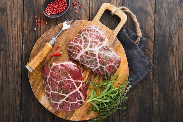 Steaks Raw Raw cowboy steak marbled beef meat with spices rosemary and pepper on black wooden board on old wooden dark table background Top view Mock up