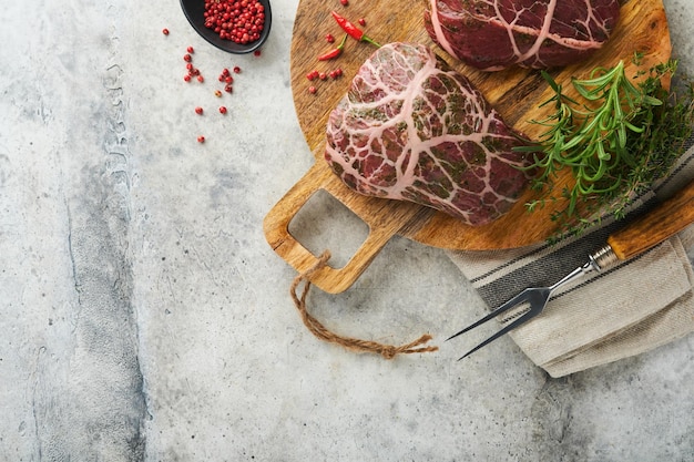 Steaks Raw Raw cowboy steak marbled beef meat with spices rosemary and pepper on old wooden board on old grey slate table background Top view Mock up