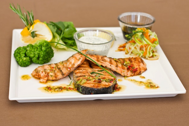 Steaks of salmon, grilled. Served with vegetables and spices on a white plate
