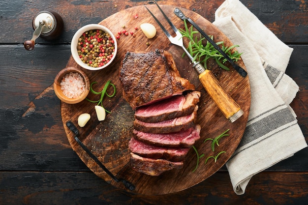 Steaks Sliced grilled meat steak New York or Striploin with spices rosemary and pepper on black marble board on old wooden background Top view Mock up