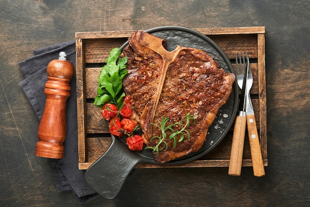 Фото Стейки tbone нарезанная говядина на гриле tbone или мясной стейк из портерхауса со специями, розмарином и перцем на черной мраморной доске на старом деревянном фоне вид сверху макет