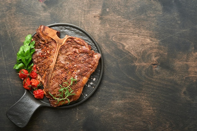 Foto bistecche tbone fette di manzo alla griglia tbone o bistecca di carne porterhouse con spezie rosmarino e pepe su tavola di marmo nero su fondo in legno vecchio vista dall'alto mock up