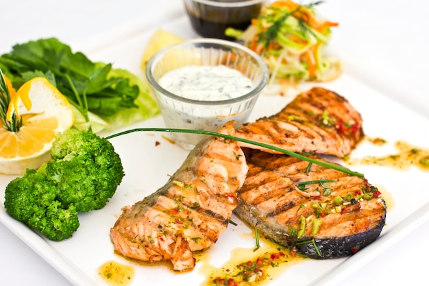 Steaks van zalm, gegrild. Geserveerd met groenten en kruiden op een witte plaat