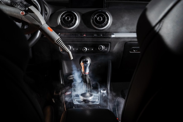 Photo steam cleaning of gearbox and dashboard in car vaping steam cleaning individual elements of black leather interior in auto creative advert for auto detailing service