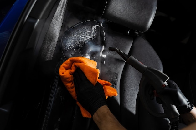 Steam cleaning of leather seat after foam washing Worker in auto cleaning service clean car inside Car interior detailing