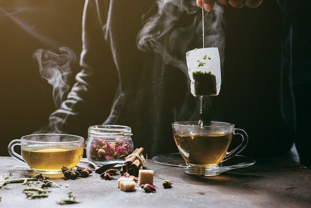 Photo the steam from man with jecket jean is soaking tea bag on vintage white cup, preparing hot tea.