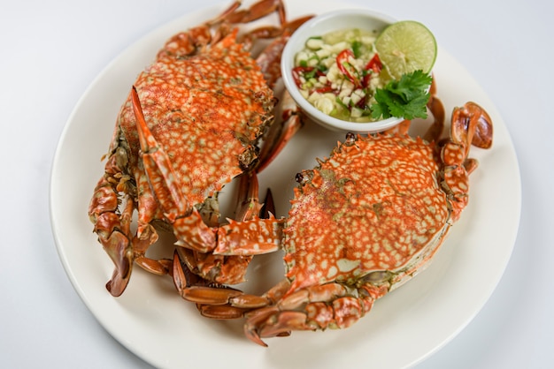 Steamed blue crab on white plate with spicy seafood sauce