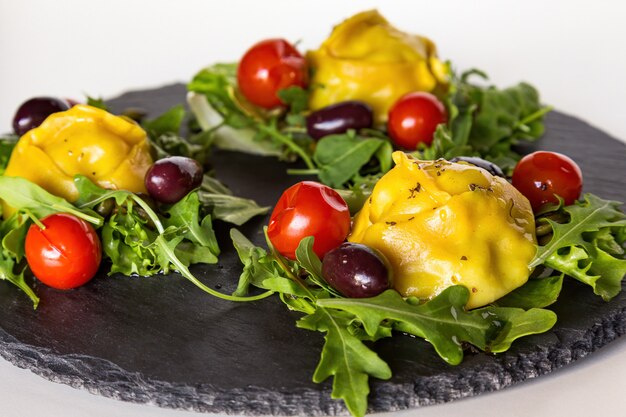 Steamed meat dumplings Manti with vegetables and greens on black stone plate.