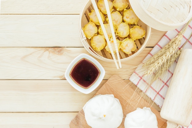 Steamed pork buns (chinese dim sum) in bamboo basket, serve with chopsticks on wooden tabl