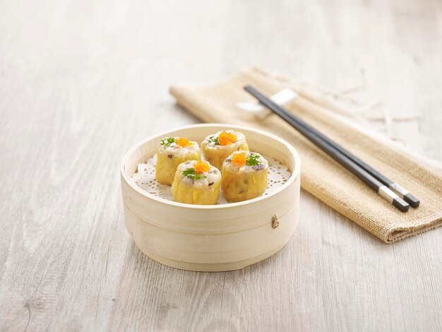 Steamed Pork Dumpling Siew Mai served in a wooden bowl with chopsticks isolated on mat side view on grey marble background